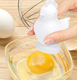 The egg yolk is seen falling out the bottom of the chicken-shaped egg separator and into a glass container.