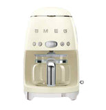 A pastel yellow coffee machine with a coffee carafe set up inside it. The base has small "feet" that elevate it slightly. The brand name "Smeg" and buttons are across the body.