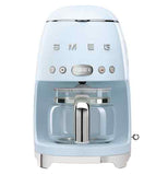 A pastel blue coffee machine with a coffee carafe set up inside it. The base has small "feet" that elevate it slightly. The brand name "Smeg" and buttons are across the body.
