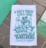 White and teal dish towel with a pirate, a mermaid, and a ship.