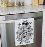 White dish towel that contain word "Momisms" and other words relating to a mother shaped like a woman in black text hanging over a dishwasher.