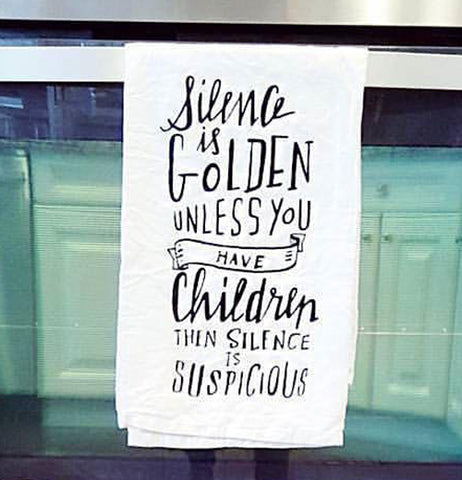 The white towel with the words, "Silence is Golden Unless You Have Children Then Silence is Suspicious" is shown hanging from the handle of an oven door.