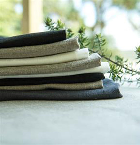 These are different color tea towels which are Black,Oyster,white and sitting on a table.