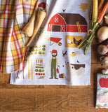 A dish towel is shown with pictures of a barn and livestock and a farmer and vegetables alongside an orange plaid dish towel and different types of vegetables.