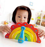 An asian child plays with a rainbow peacock toy in a playroom.  It's red, orange, green, and blue.