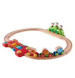 A wooden toy train track is assembled in a cirle. There is a red bridge to the left, with blue, green, orange, and yellow tracks. Brown monkeys are on the right of the track, in a green structure. A tiger, lion, and elephant are on red and yellow, green and red, and blue and green cars, respectively.