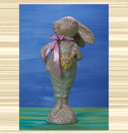 A statue of a smiling beige bunny with a pink ribbon.