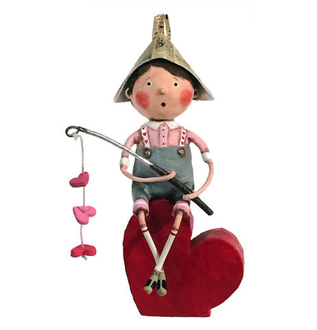 Fishing boy is holding a fishing pole with three hearts on it and sitting on a heart. He has a paper hat on with a pink shirt blue shorts.