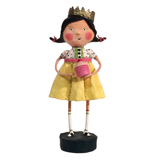 The queen is wearing her gold crown and yellow dress with pock a dots and white socks. She is holding a pink cup cake. 