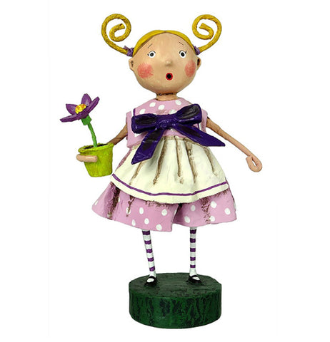 This figurine is of a girl with her blonde hair in pigtails wearing a pink dress with white polka dots. She also wears a dark purple bowtie and holds a potted purple flower in her left hand. 