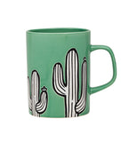 Green porcelain mug with white and black cactus design on a white background.
