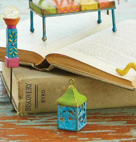 The "Mini Bird Lantern" sits on the table with the "Mini Lamp Post" standing against the closed book and the "Mini Bench" sitting on the opened book.