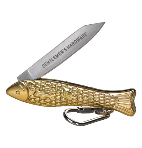 Close-up of a gold pocket knife shaped like a fish with the silver blade that's engraved with the words "Gentlemen's Hardware" opened to a 45 degree angle. Under the tail of the fish is a silver key ring and carabiner.  