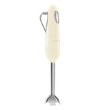  The side view of this cream colored hand blender shows the on/off button and the half logo of SMEG and on the left he grey power cable, the base part is silver.