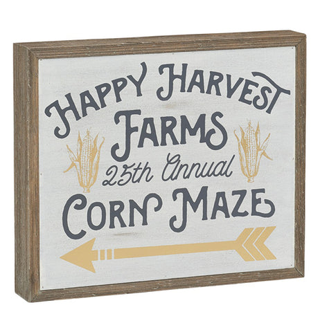 a box sign that says "happy harvest farms", 25th annual" and "corn maze" on it with pictures of gold corn in their husks and a gold arrow