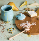 Wooden serving tray with cheese, honey pot, lid and honey dipper.