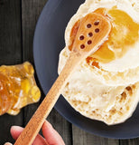 The wooden spoon is shown spreading honey on some pancakes.
