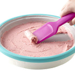 The spade-shaped magenta scoop taking a thin roll out of a sheet of ice cream inside the turquoise edged pan