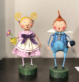 The blue dressed figurine is shown standing on a shelf next to a girl figurine wearing a pink dress with white polka dots and holding a potted flower. 