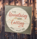 The silver wooden box with the words, "The Mountains Are Calling And I Must Go" in grey and orange red lettering resting against a dark brown wooden background.