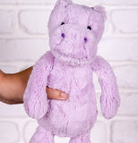 a plush lilac hippo being held up against a brick back ground.