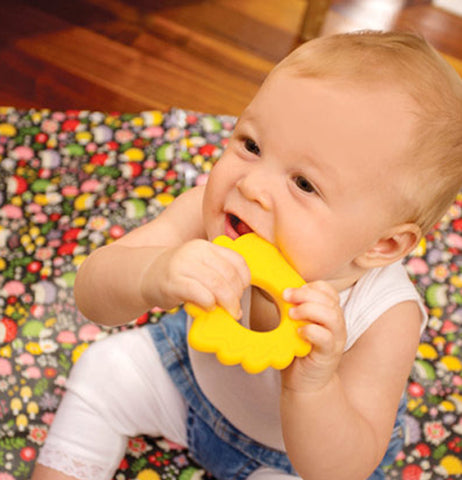 The baby chewing on a "Hedgehog" teether while sitting on the "Hedgehog" Jumbo Floor Splat Mat. 