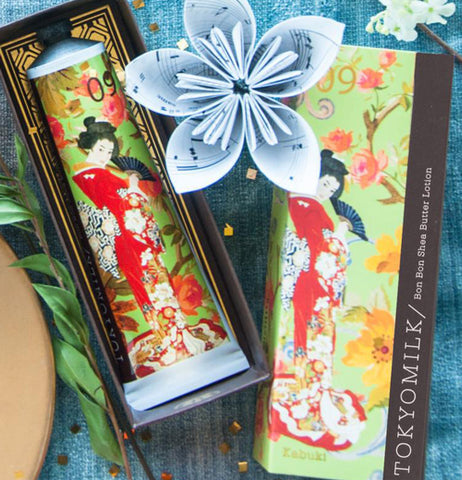 Handcreme with image of a Kabuki dancer dressed in red and white holding a black dancer fan inside its case with a white flower next to it and the box shell next to it. 