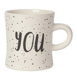 White mug that reads "You" in black with black specks over a white background.