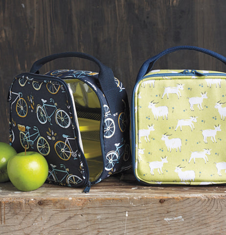 The blue lunch bag covered with bicycles is shown open with a green apple sitting on its left. To the right of the image is another lunchbox with goats against a green background.