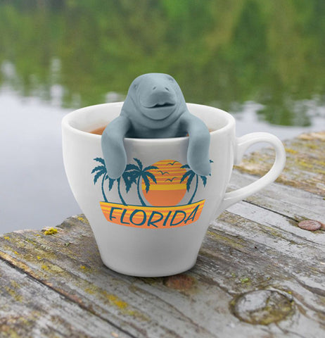 The "Mana Tea" Infuser gripping the inside rim of a Florida tea cup on a deck close to the pond. 