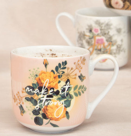 The "Make it Strong" mug is next to another mug on a pink tablecloth.