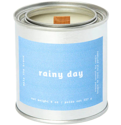 A gray tin candle-shaped can with a pastel blue label. The label says "Mala the brand--rainy day--Net weight 8 oz. -- scented coconut soy candle." There is also French text, but this alt text writer is woefully monolingual.