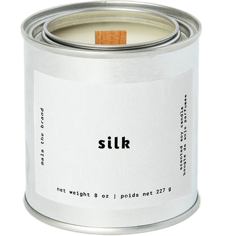 A gray tin candle-shaped can with a white label. The label says "Mala the brand--silk--Net weight 8 oz. -- scented soy candle." There is also French text, but this alt text writer is woefully monolingual.