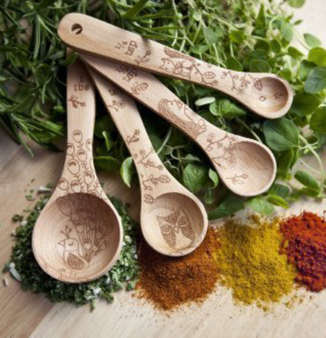 The four measuring spoons are shown lying on top of some vegetables with a few different spices lying underneath them.