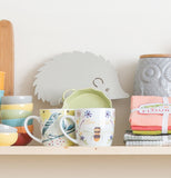 a mug with a beee on it sits on a shelf along side a hedgehog trivet and a couple of small bowls