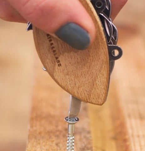 The screwdriver tool on the crab-shaped Swiss army knife is shown screwing a screw into some wood.