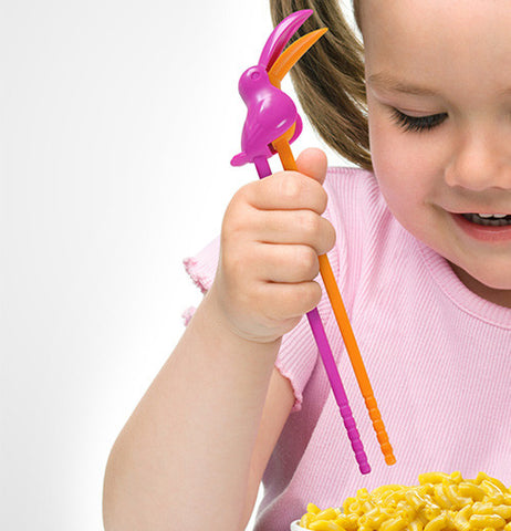 A little girl using the toucan shaped chopsticks for her noodles