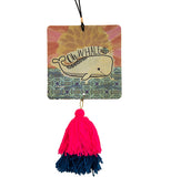 A square shaped mutli-color air freshener has a whale design printed on it. It has an elastic hanger with a wooden bead on top, and a pink and blue yarn tassel hanging off the bottom. Text reads "Oh whale."