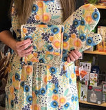 A woman is shown holding the floral mitts while wearing a similarly designed apron.