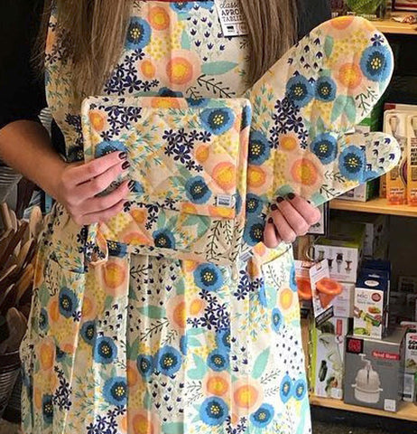 A woman is shown holding the floral mitts while wearing a similarly designed apron.