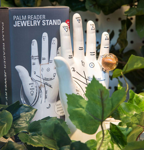 The Palm Reader Jewelry Stand and its packaging both sit in a garden.