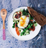 The spoon with the words, "Pass it On" is shown sitting on a table next to some eggs, steak, and broccoli.
