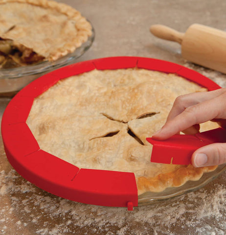 A picture of a person's hand placing the pie shield on the pie. 