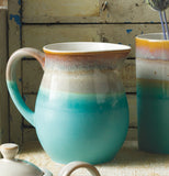 Reactive glaze horizon pitcher that is turquoise at the bottom with dark beige in the middle and caramel color on top in a wooden background