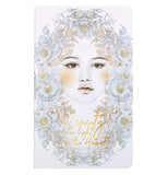 This notebook features a woman's face in black and white with a surrounding blue, gray, and gold floral print with the words "Beauty in a Light in the World"