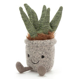 "Aloe" silly succulent with a smiley black face over a gray felt pot for a body with long green jersey leaves pointing out from brown felt soil with brown feet sticking out.