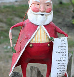 The Santa Claus figurine with the monocle and Christmas list is shown standing with a green hill behind him.