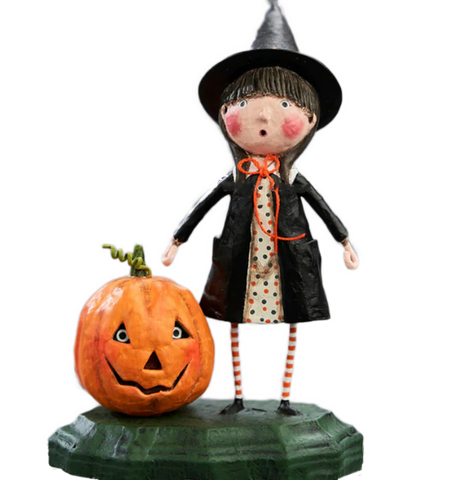 This figurine shows a young girl in a witches costume and pointed hat, standing next to a pumpkin