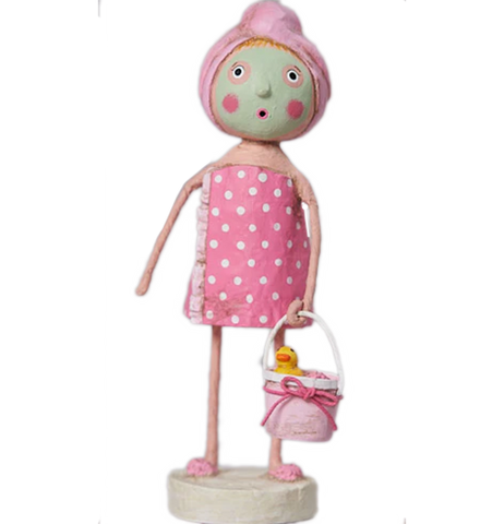 A rosy cheeked girl wears a green face mask and pastel pink towel. She is wearing a pink towel around her body, pastel pink slippers, and carries a white and pastel pink with a pink bow around it. The bucket has a yellow rubber ducky with an orange bill.