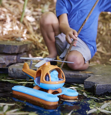 A little boy playing with his helicopter in a pond.